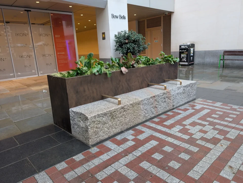Bow Churchyard Phase 1 — reclaimed granite slab seating with Corten steel raised planter and brass armrests, outside Bow Bells House